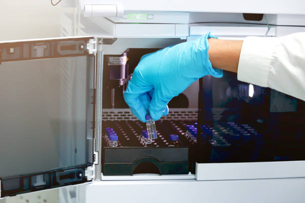 mão do cientista da pesquisa com as luvas que prendem o frasco (frasco pequeno) para põr a bandeja dentro da seção da injeção do instrumento líquido da cromatografia do elevado desempenho (hplc), experiência analítica da química - hplc - fotografias e filmes do acervo