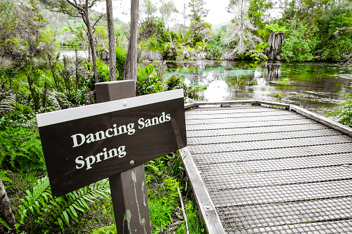 Dancing sands spring sign Te Waikoropupu Springs, Pupu Springs, Golden Bay, New Zealand: crystal clear water flows from subterranean underground spring wells to this central overflow blue lake with beautiful green landscape