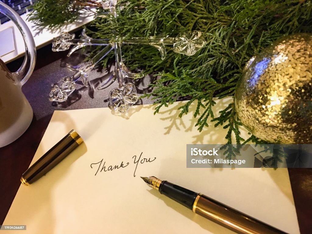 Christmas card writing thank you with evergreen  and ornaments background Christmas time and holiday season writing cards with elegant fountain pen and words Thank You in background on desk with coffee, crystal and gold ornaments and fresh evergreen branches Thank You - Phrase Stock Photo