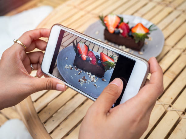 main de femme prenant une photo de la tarte délicieuse de chocolat sur le plat en céramique par le smartphone dans le café. - tart dessert chocolate fruit photos et images de collection