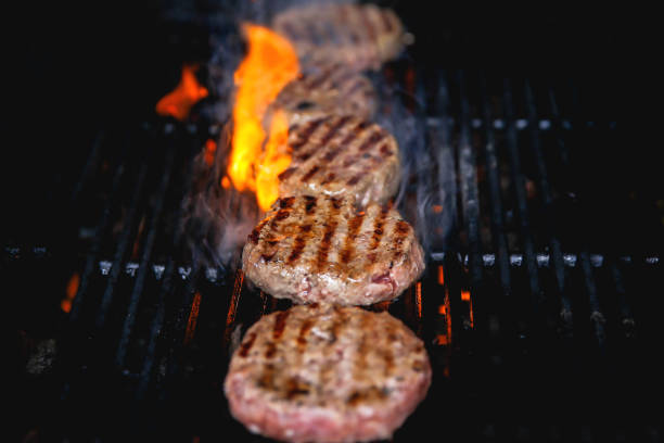 Close up grilling beef burger patties on barbecue grill,with fire flaming into the meat.