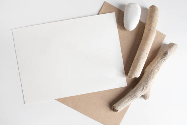 Mock up of postcard among rustic sticks and brown craft envelope on white table. Boho design of postcard on white table with copy space for your image or text stock photo