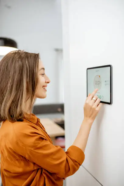 Young woman controlling temperature in the living room with digital touch screen panel. Concept of heating control in a smart home