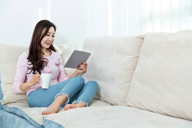 istock Beautiful woman sitting on the sofa and using digital tablet 1193452995