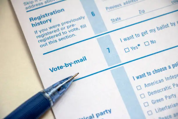 Closeup of voter registration form, focused on the Vote-by-Mail section with pencil on top.