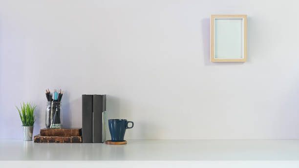 istock Comfortable workspace with books, pencil, coffee, plant and photo frame on white table and white wall. 1193457512