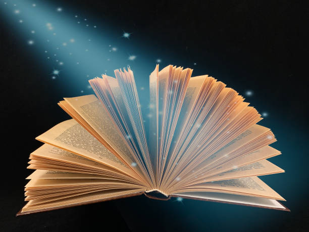 istock Ajar pages in the book. Old hardback textbook, on black background. Concept: education, training, love of knowledge. 1193462769