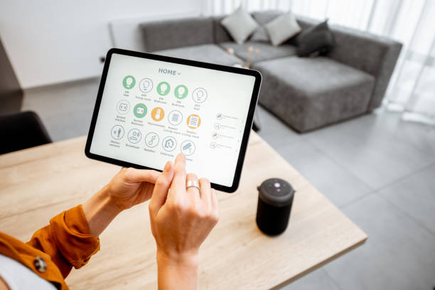 Woman controlling smart devices with a digital tablet at home Young woman controlling home with a digital touch screen panel. Concept of a smart home and mobile application for managing smart devices at home home automation stock pictures, royalty-free photos & images