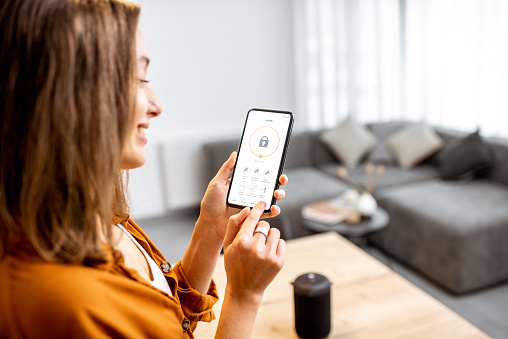 Young woman holding smart phone with launched security application at home. Concept of controlling and managing home security from a mobile device