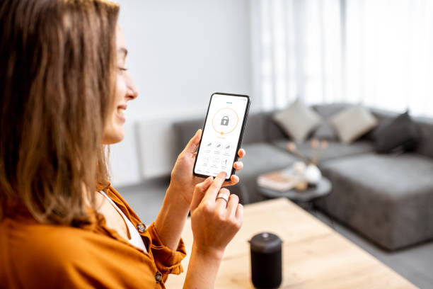 Woman controlling security from a mobile device Young woman holding smart phone with launched security application at home. Concept of controlling and managing home security from a mobile device looking at cell phone screen stock pictures, royalty-free photos & images