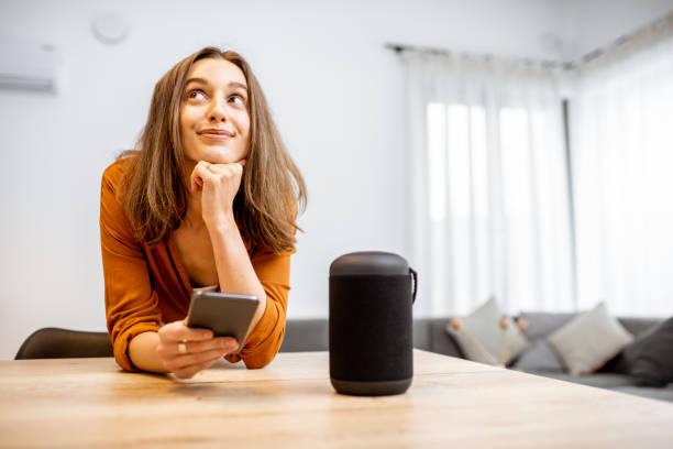Woman with smart wireless column at home Portrait of a young and cheerful woman with a smart wireless column and phone at home. Concept of smart home and voice command control home automation stock pictures, royalty-free photos & images