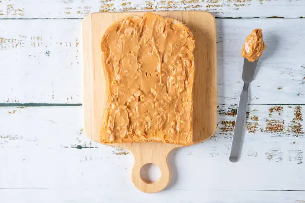 Photo of Creamy and smooth crunchy peanut butter sandwich or toast on white wood table. Natural nutrition and organic food. Top view.