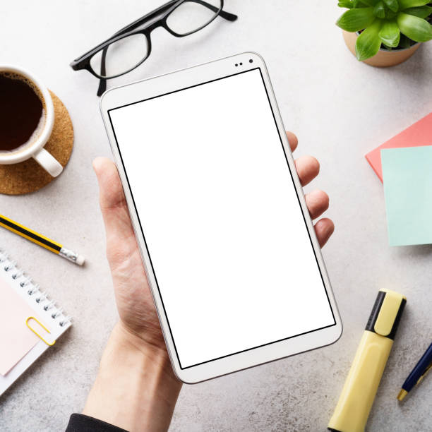 istock Male hand holding a device with white blank screen over a desk. 1193476572