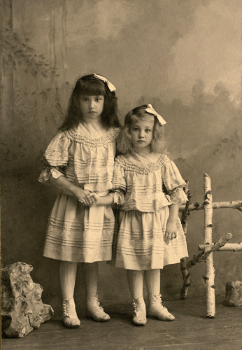 Vinatge photo of a small boy, aged 5 years. Circa 1933. Interior shot with the child seated on an ornate wooden bench, with draped curtain background.