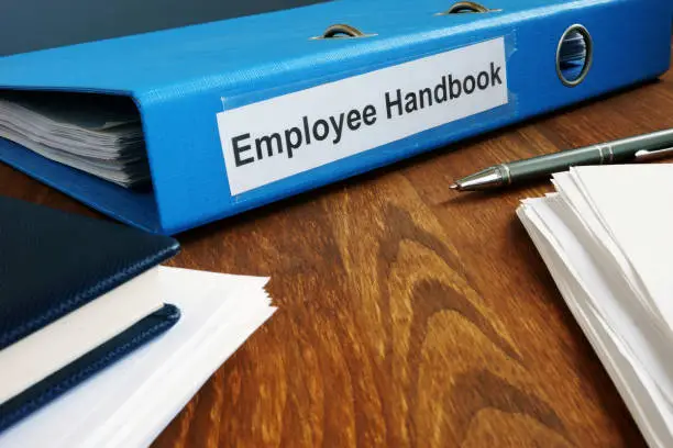 Photo of Employee Handbook manual in folder and documents.