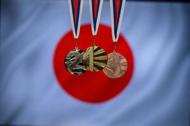 Photo of Silhouette of tree medal: Gold, Silver an Bronze. Japan flag in background.