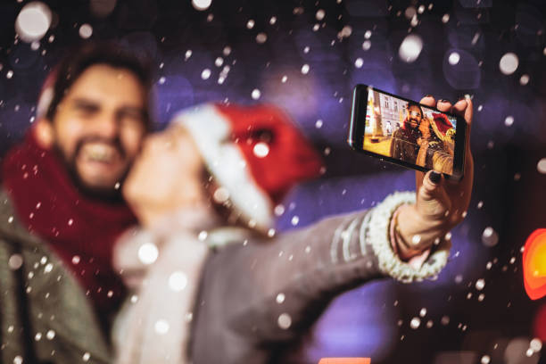 Happy young loving couple making selfie and smiling while standing Christmas background