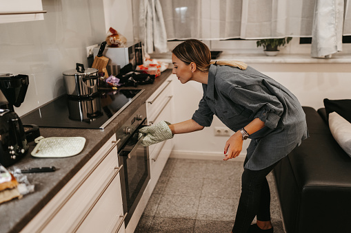 Young woman in kitchen opening oven to check meal