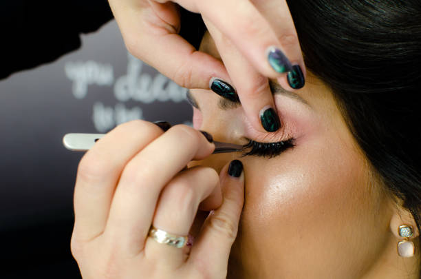 istock Make-up artist working with tweezers putting false long black eyelashes on female client in beauty studio. 1193486792