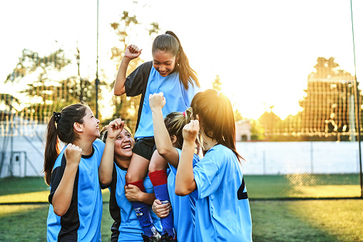 Cheerful girls carrying player on shoulders after winning match. Female soccer team is celebrating success. They are enjoying together on field.