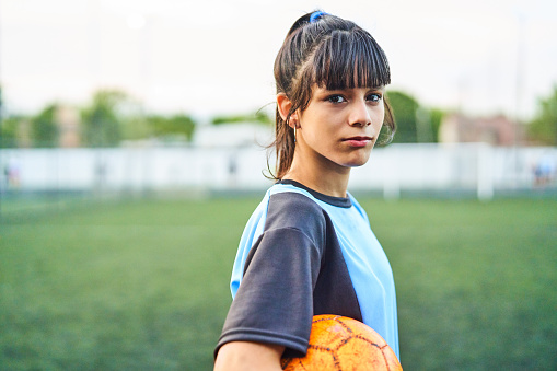 Side view portrait of soccer girl holding ball. Confident female player is on sports field. She is in sportswear.