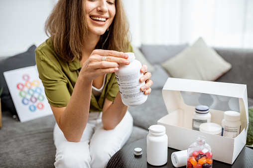 Woman taking vitamins or nutritional supplements in the form of pills while sitting on the couch at home. Concept of biohacking and preventive medicine