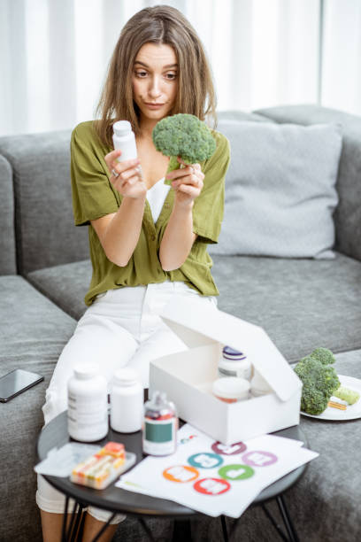 Thoughtful woman with nutritional supplements and broccoli at home