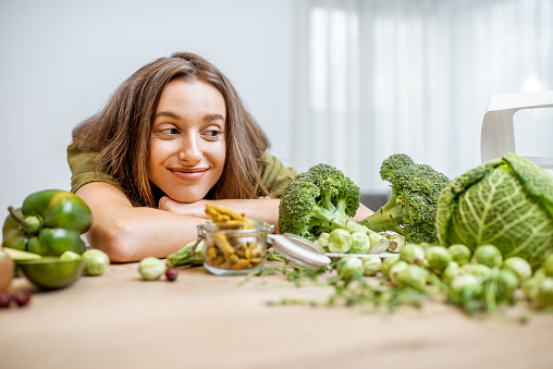 Portrait of a young cheerful woman with lots of healthy green food on the table. Concept of vegetarianism and well-being