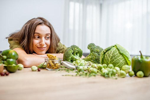 Portrait of a young cheerful woman with lots of healthy green food on the table. Concept of vegetarianism and well-being