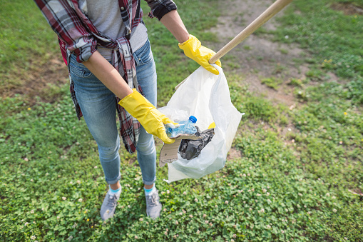 Young female volunteer cleaning the environment in the park, collecting litter in garbage bags