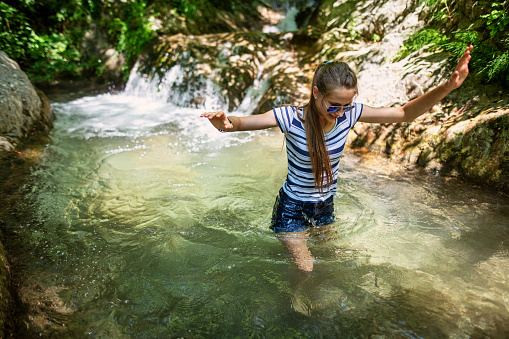 Family hiking in Campania, Italy. It is very hot day and teenage girl is walking in clothes to a cold mountain stream to cool down.\nNikon D850