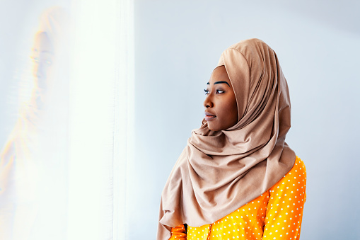 African-American Muslim woman looking from hotel apartment window