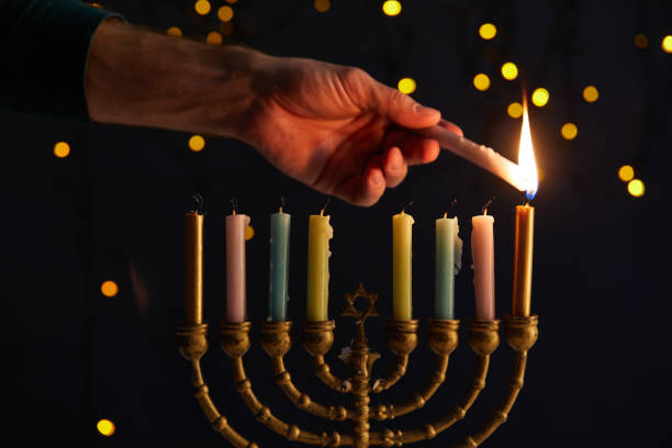 vista parcial del hombre encendiendo velas en menorah sobre fondo negro con luces bokeh en hanukkah - menorah fotografías e imágenes de stock