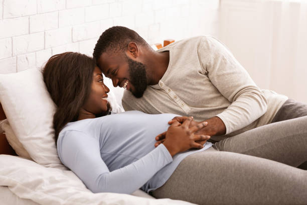 pregnant couple in love cuddling in bed at home - sexuality imagens e fotografias de stock