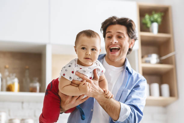 istock Cheerful daddy riding his baby son like plane, kitchen interior 1193497095