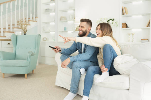 young spouses watching tv, excited woman pointing at screen - apartment television family couple imagens e fotografias de stock