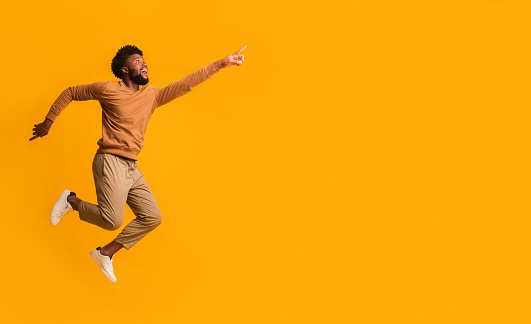 Magnetic offer. Excited afro man pointing and running towards copy space, orange studio background