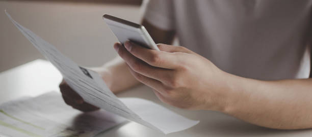 istock panoramic banner. young man using mobile smart phone for scan and payment online with family budget cost bills on desk in home office, money cost saving, investment, business finance, expenses concept 1193499735