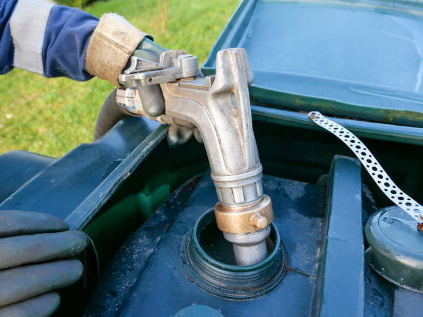 A home delivery of heating oil in a rural location An oil delivery driver filling up a residential oil tank. He is delivering to a rural location in Scotland, where mains gas is not connected. The man is wearing protective overalls and gloves as he carefully fills the green plastic tank with home heating oil, in preparation for the winter months. He is squeezing a metal nozzle attached to a long rubber hose that runs from his oil delivery lorry parked nearby to maintain control of the amount being delivered. fuel storage tank photos stock pictures, royalty-free photos & images