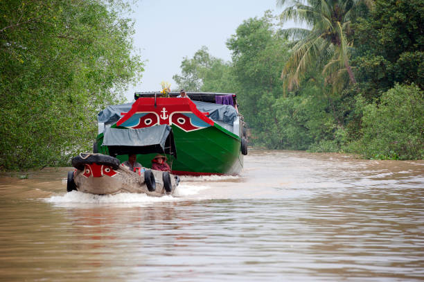 It's behind you! Mekong Delta traffic, South Vietnam Water traffic, Mekong River, South Vietnam. Water craft traffic such as barges, houseboats, passenger craft, industrial freighters and small personal boats travel the green rippled waters of the channels and routes of the mighty Mekong River as it flows to the Mekong Delta, South Vietnam small houseboats stock pictures, royalty-free photos & images