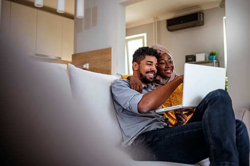 Young African-American Muslim couple sitting and relaxing on sofa with laptop. Love, happiness, people and fun concept.
