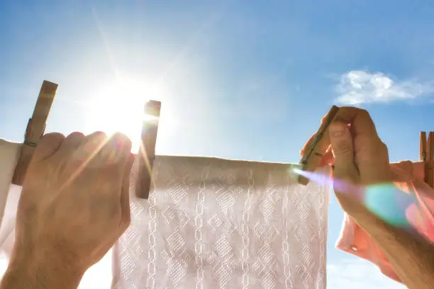 A pair of hands reaching up to hang a white shirt on a washing line