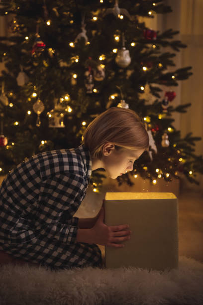 istock Cute little boy in his pajamas looking at the magic light going from the present box in front of decorated Christmas tree 1193502713