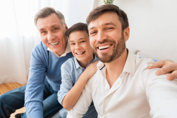 istock Man with son and father making selfie sitting on sofa 1193504112