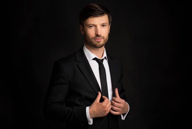 istock Businessman Holding Jacket Lapels Looking At Camera Standing, Black Background 1193504210