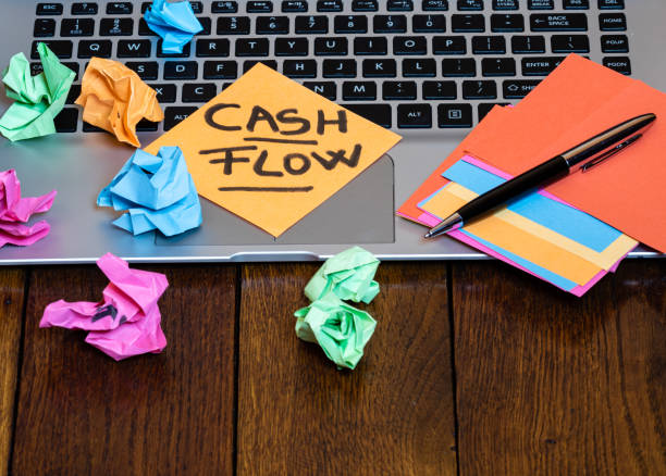 istock Different objects on wooden office desk. Modern wooden office desk table with laptop keyboard, pen, blank colorful sticky notes, black glasses, crumpled paper and post it with text Cash flow. 1193509126