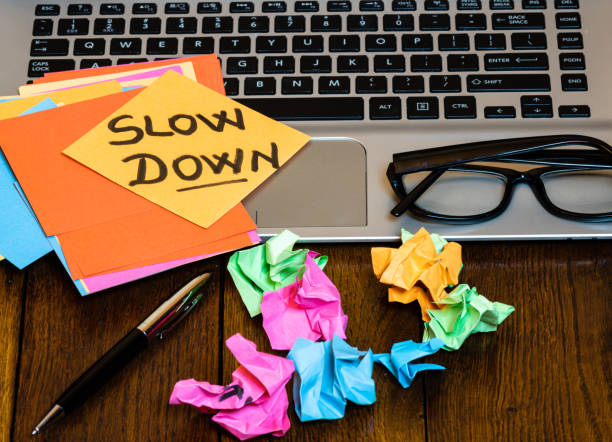 istock Different objects on wooden office desk. Modern wooden office desk table with laptop keyboard, pen, blank colorful sticky notes, black glasses, crumpled paper and post it with text Slow down. 1193509211