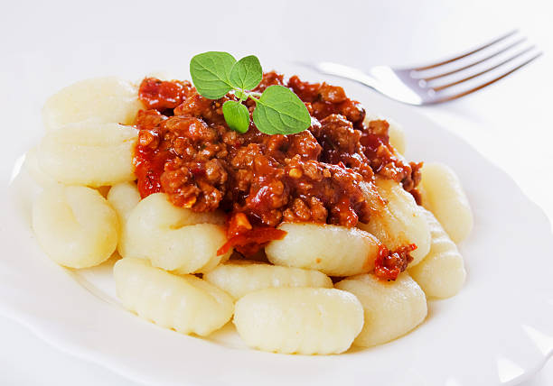 Stock photo shows a close-up of a person eating Italian food, enjoying gnocchi with tomato ragu sauce, spinach, and grated Parmesan cheese. Soft potato dumplings in a rich, savory sauce highlight authentic Italian cuisine, fresh ingredients, and homemade comfort food