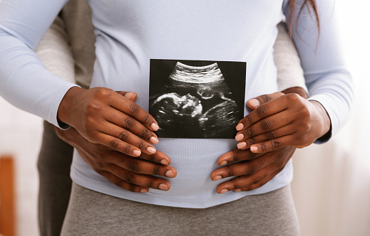 Waiting for baby. African couple holding sonogram picture in front of woman belly, cropped