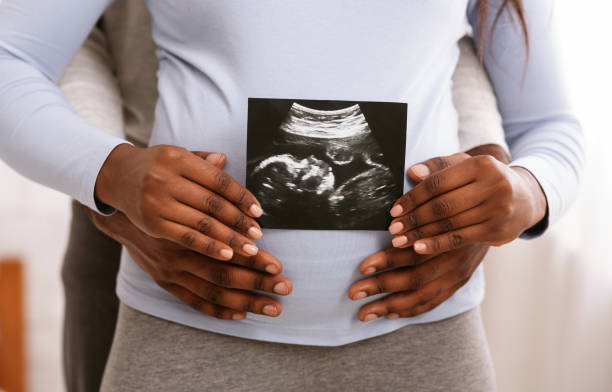 Black couple holding ultrasound image in front of woman belly Waiting for baby. African couple holding sonogram picture in front of woman belly, cropped fetus photos stock pictures, royalty-free photos & images